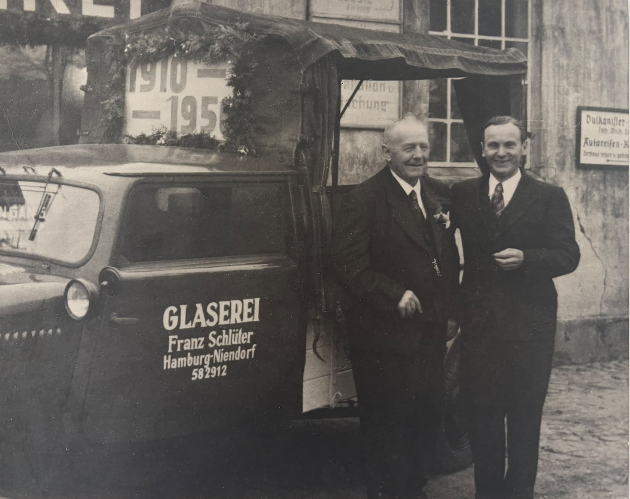 Historisches Foto zweier Männer vor dem Lieferwagen der Glaserei Franz Schlüter in Hamburg-Niendorf, am Wagen die Jahre 1910 bis 1950